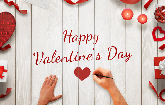 Man hand painting  Happy Valentines day message on a wooden background. Love decorations beside, gifts, candles, hearts