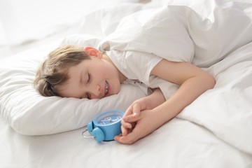 Happy smiling sleeping little boy with alarm clock near his head