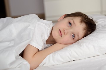 7 years old boy resting in white bed with eyes open