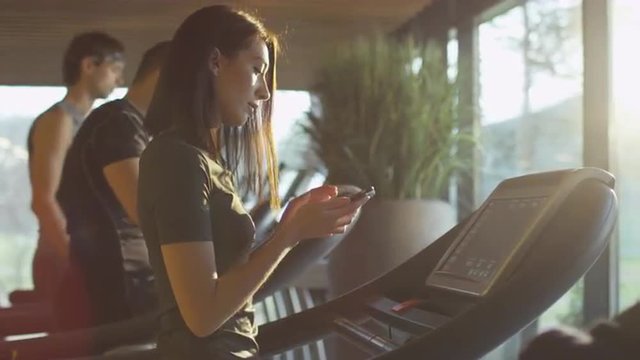 Attractive caucasian girl is starting to run on the treadmill in the sport gym with earphones. Shot on RED Cinema Camera.