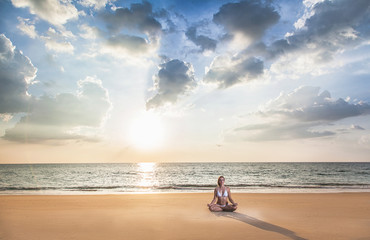Young woman practicing yoga on the beach at sunset. Healthy active lifestyle concept.