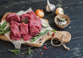 Fresh raw chopped beef on an olive board, spices, herbs and vegetables on dark wooden background....