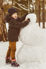 The concept of winter activities . Happy boy making snowman outdoor