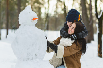 Happy family in warm clothing. Smiling mother and son making a snowman outdoor. The concept of winter activities