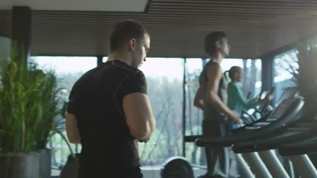 Fit athletic man is starting to run on the treadmill in the sport gym with earphones. Shot on RED Cinema Camera.