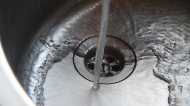 Leitungswasser str&ouml;mt in Waschbecken aus Edelstahl und flie&szlig;t ab