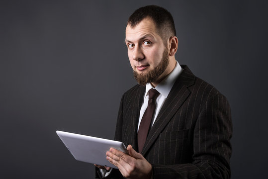 Bearded businessman with a tablet on grey background