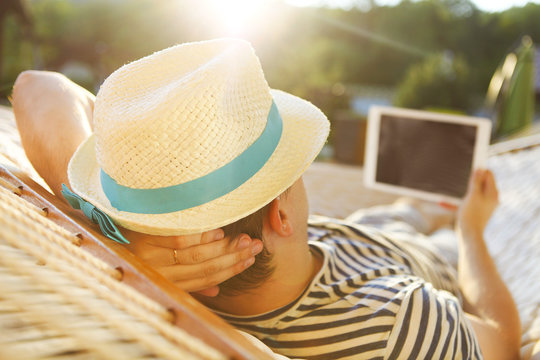 Man In Hat In A Hammock With Tablet Computer On A Summer Day