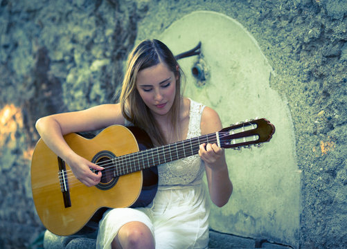 Beautiful young blonde girl with white dress playing a guitar in a sunset scenario