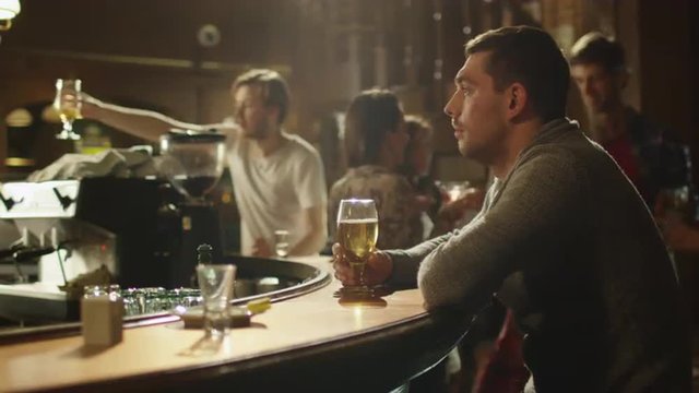 Man sitting alone with beer in a bar while people are having good time. Shot on RED Cinema Camera.