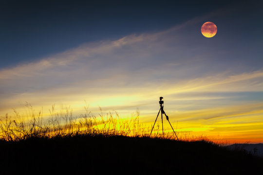 Tripod stand on mountain with moon at after sunset.