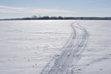 Snowmobile tracks race off to the horizon across the flat snow and ice of a lake.