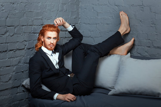 On the sofa with his feet is fashionable guy.