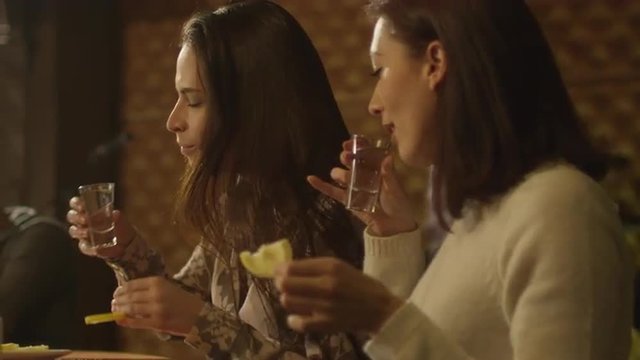 Two girls are sitting at a table and drinking tequila while having a good time together at a bar. Shot on RED Cinema Camera.
