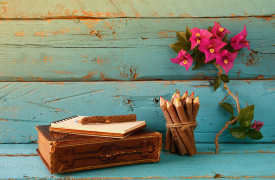 vintage notebook and stack of wooden colorful pencils on wooden texture table next to purple bougainvillea flower. vintage filtered and toned image