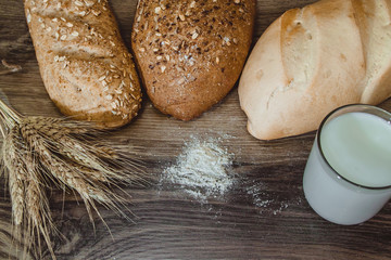 Breads assortment with wheat and glass of milk on a wooden table