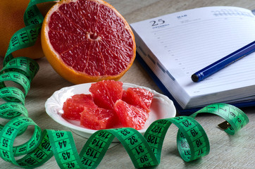 Slices of grapefruit, measuring tape and notebook on the table