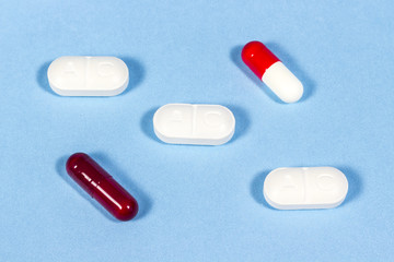 Generic tablets of clavulanic acid beside hard gelatin capsules, on blue floor. Antibiotic drugs