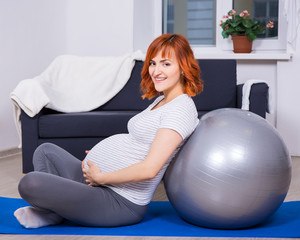 happy pregnant woman doing exercises with fitball in living room