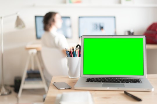 Green screen laptop computer and a glass with color pencils on wooden table, creative office on the background