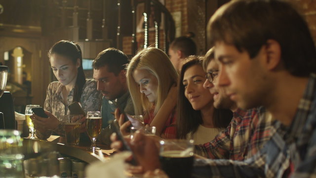 Friends laugh, use smartphones while having a good time together at a bar. Shot on RED Cinema Camera.