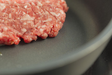 Red raw burger on a black pan close up