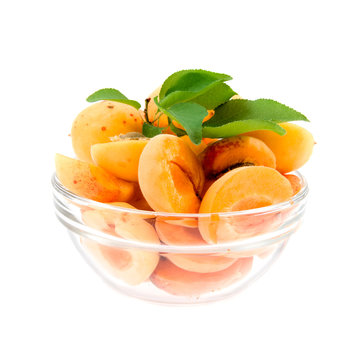 apricot halves with leaves in a transparent plate on a white bac
