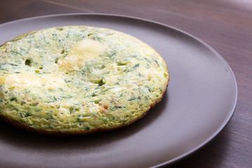 Omelet with spinach and zucchini with melted cheese on brown pla