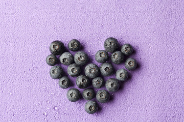 Blueberries heart on purple background from above