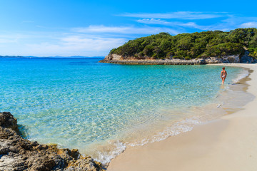 Unidentified woman walking along sandy Petit Sperone beach with azure sea water on coast of Corsica island, France