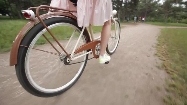 Девушка с длинными волосами в платье едет на велосипеде в парке