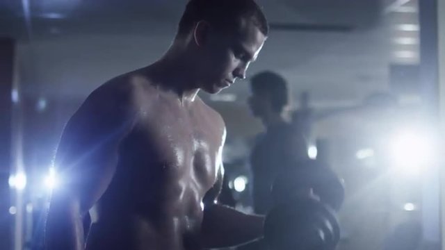 Handsome fit sporty man without shirt does dumbbell curl exercises in the gym. Shot on RED Cinema Camera.