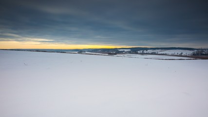 Winter field landscape under cloudy sky.
