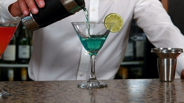 Barman pouring cocktail into glass 