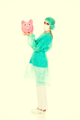 Female surgeon doctor holding piggy bank