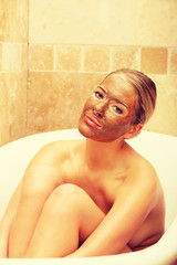 Woman sitting in a bath with face mask