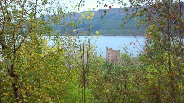 A view through the trees of a beautiful Scottish castle overlooking a lake.