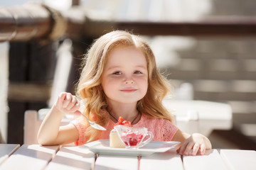 Little girl eating cake with strawberries in the summer cafe