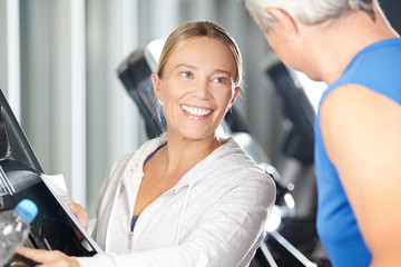 Fitnesstrainer hilft Senior am Laufband