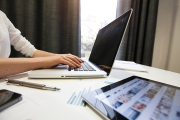 Woman using a laptop next to a window with tablet pc and smartph