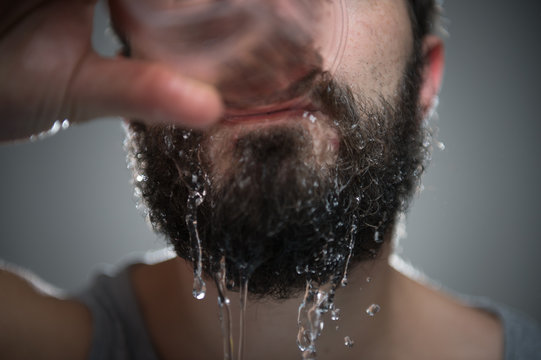 Junger Mann trinkt Wasser und macht sich dabei nass