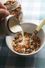 Healthy eating, muesli and milk for breakfast. Pouring milk over muesli in a bowl.
