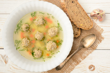 Dietary soup with meatballs and vegetables on white wooden table.