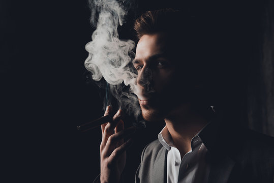 Handome man in suit on the black background smoking a cigar