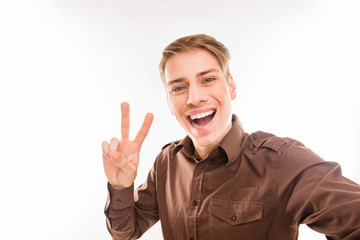 Cheerful young man making selfie and gesturing with two fingers