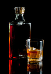 bottle and glass of whiskey with ice on dark background
