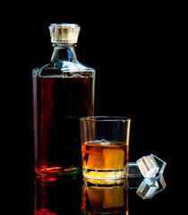 bottle and glass of whiskey with ice on dark background