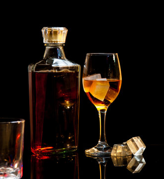 bottle and wineglass of whiskey with ice on dark background