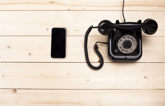 Old retro black phone and new cell phone on wooden board, top view, DOF, focus on phone