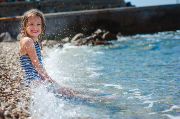 happy child girl in swinsuit relaxing on the beach and playing with water. Summer vacation at sea.